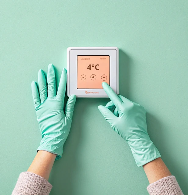 Deux mains gantées ajustant un panneau de contrôle de température numérique affichant 4°C sur un mur vert clair.